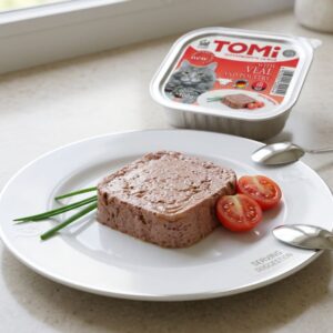 מעדן פטה לחתולים טומי (TOMi) בטעם עגל ועוף במגשית אלומיניום 100 גרם, מוגש על צלחת לבנה מעוצבת.
