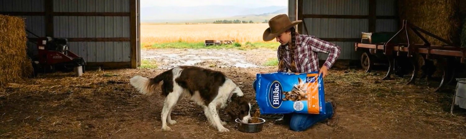 אישה בחווה מאכילה כלב מגזע גדול במזון יבש Bil-Jac Large Breed Adult.
